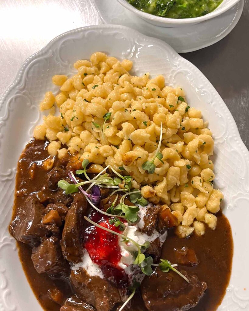 Hausgemachtes Wildragout mit Spätzle, Preiselbeeren und Sauerrahm, serviert auf einem weißen Porzellanteller – fränkische Spezialität im Brauereigasthof Werneck.