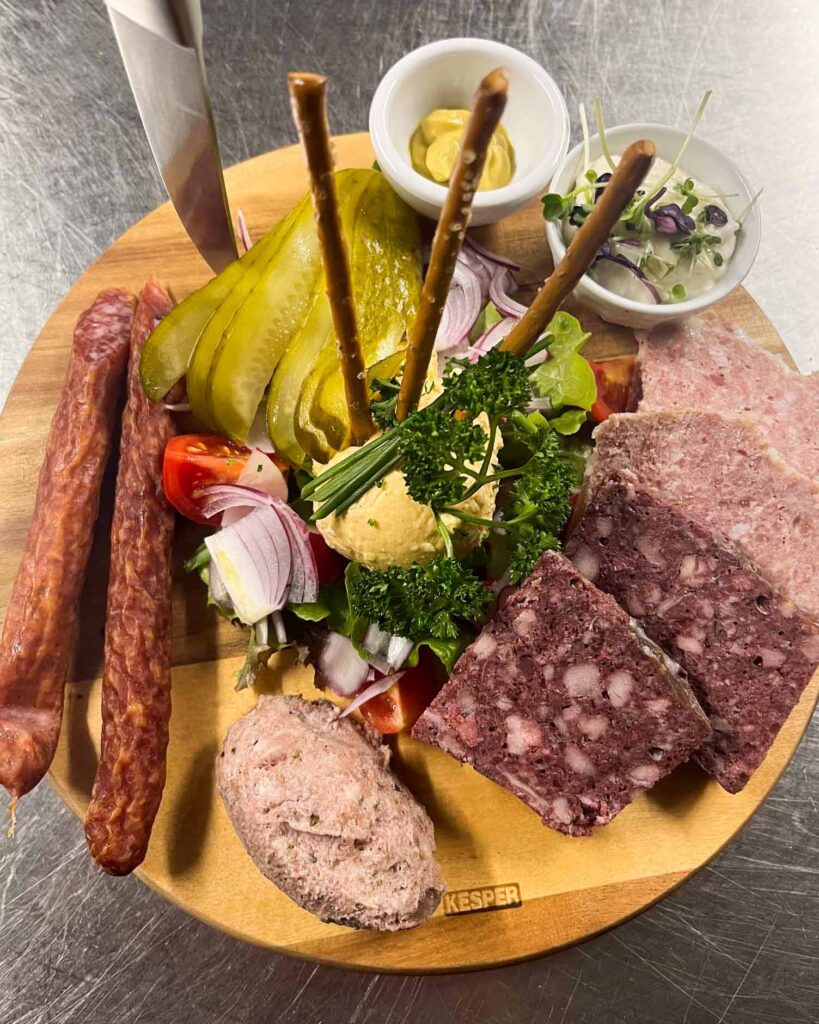Deftige Brotzeitplatte mit Hausmacher Wurst, Presssack, Obazda, Essiggurke, Zwiebeln und Bauernbrot – serviert im Brauereigasthof Werneck.
